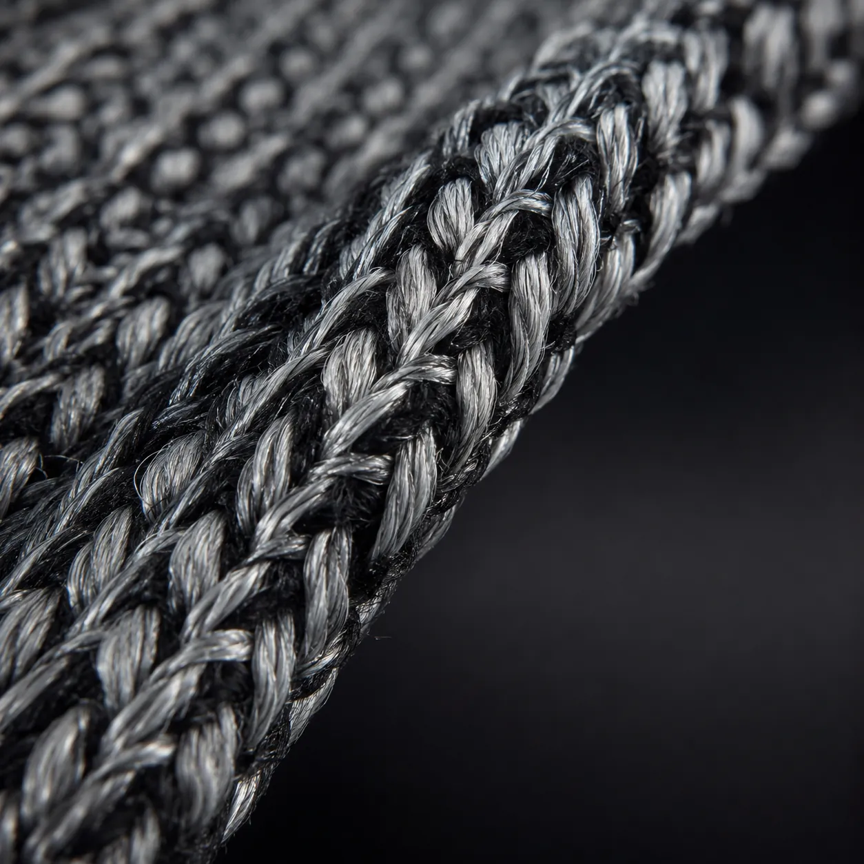 Macro shot of the protective knit, with silver-grey high-performance yarns interlocked with fine black fibers.